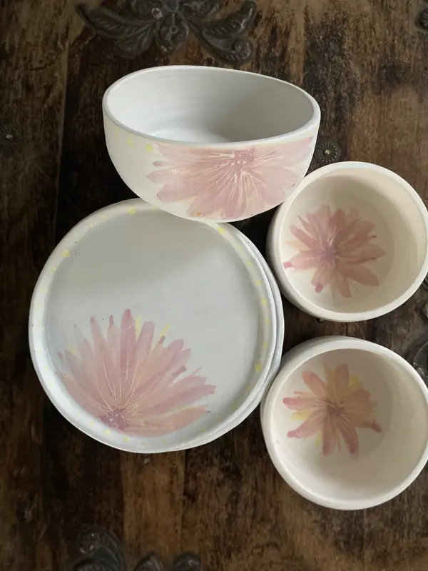 Four white ceramic bowls and plates featuring hand-painted pink floral designs on a dark wooden surface.