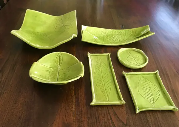 Collection of apple green ceramic bowls and trays with hand-carved leaf patterns on a wooden surface.