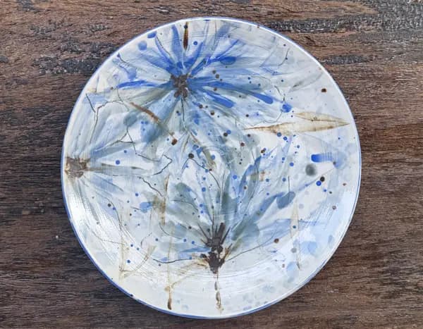 Hand-painted ceramic plate with abstract blue flowers and brown accents on a white glaze.