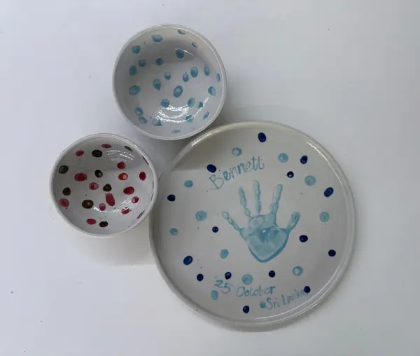 Ceramic set featuring two small dotted bowls and a commemorative plate with a blue handprint and inscription.