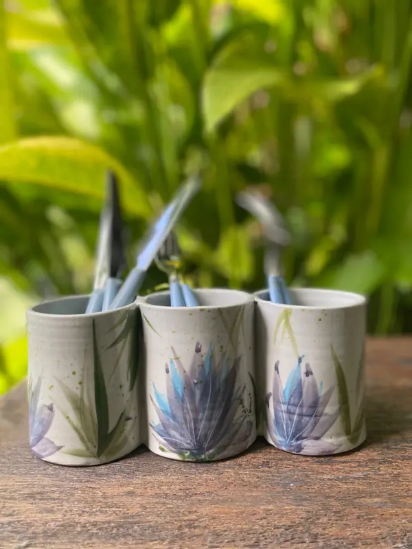 White ceramic triple cutlery holder with painted blue and purple floral motifs on a wooden table.