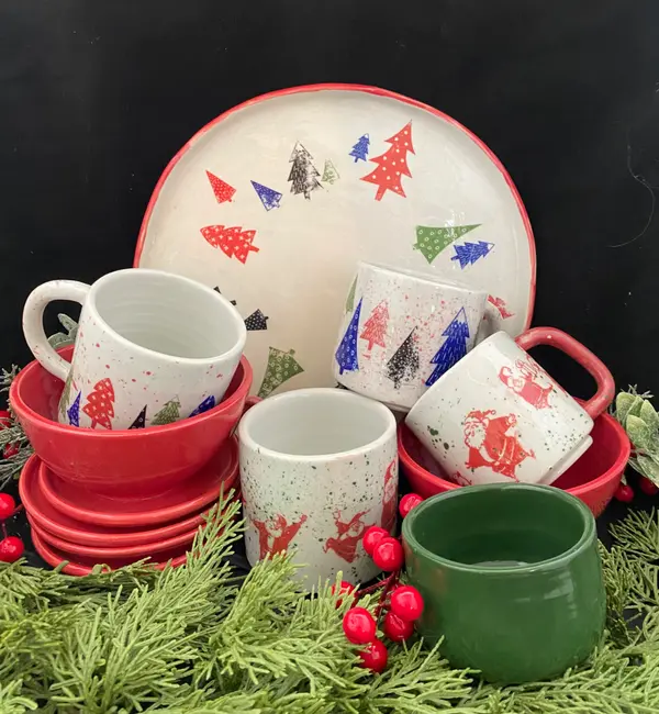 Festive pottery set with Santa and Christmas tree patterns, featuring mugs, bowls, and a platter on pine branches.