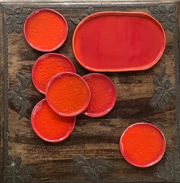 Vibrant red textured ceramic platter and several small round plates arranged on a dark carved wooden surface.