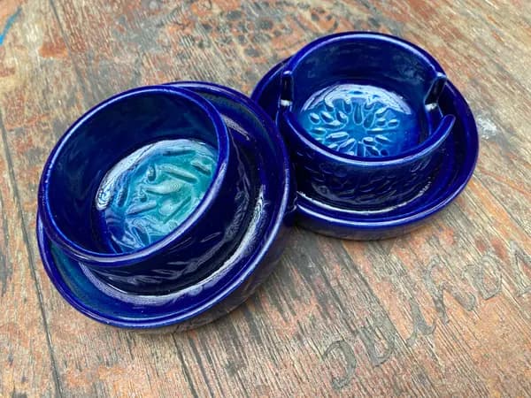 Two glossy cobalt blue ceramic dip bowls with stamped patterns and turquoise interiors on a wooden surface.
