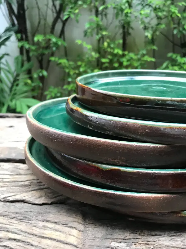 Stacked handmade ceramic plates with glossy green glaze and dark brown textured rims on a wooden surface.