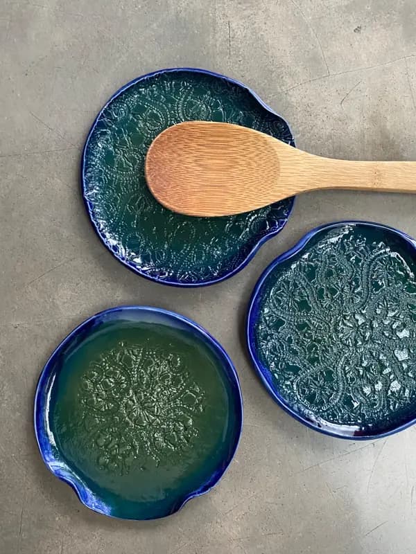 Trio of ceramic spoon rests with lace patterns, glazed in deep cobalt and green, holding a wooden spoon.