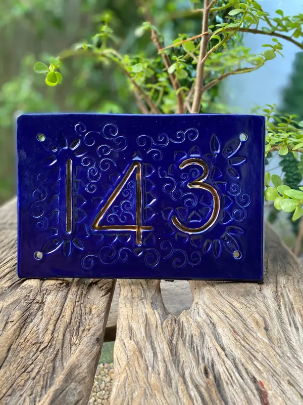 Cobalt blue ceramic house number plaque with gold relief numbers 143 and intricate scroll textures.