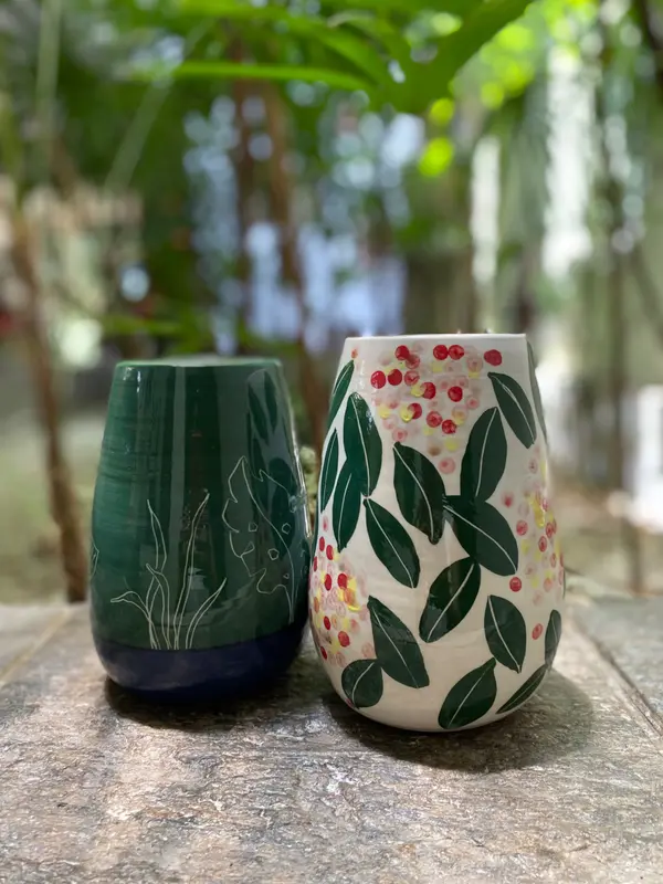Two hand-painted ceramic vases with botanical motifs, one dark green and one white, on a stone surface.