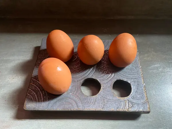 A dark, textured ceramic egg holder with four brown eggs, featuring a circular wave pattern and dramatic lighting.