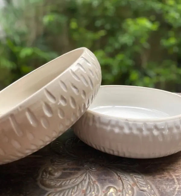 Two beige ceramic bowls with carved teardrop textures on the exterior, resting on a rustic surface.