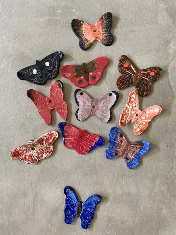 A collection of colorful hand-painted ceramic butterflies and moths with unique patterns on a neutral background.