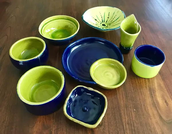 A collection of handmade cobalt blue and apple green ceramic bowls and plates on a dark wooden table.