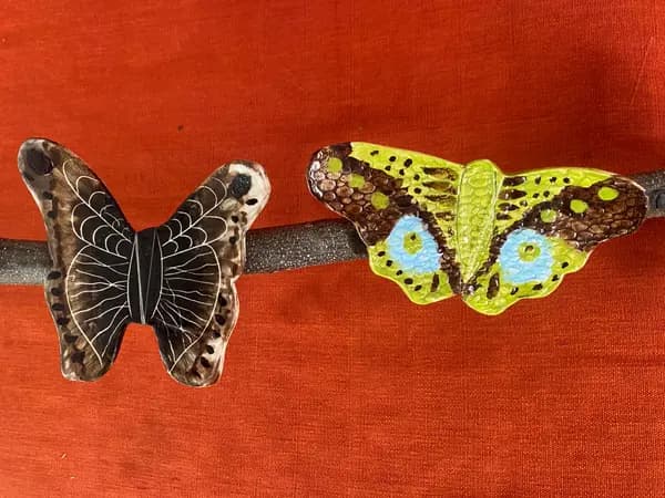 Two ceramic butterflies, one brown and white and one green and brown, mounted on a dark branch.