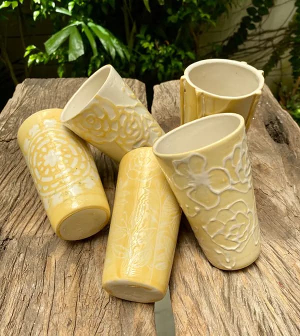 Five yellow ceramic tumblers with white floral and geometric patterns on a weathered wooden surface.