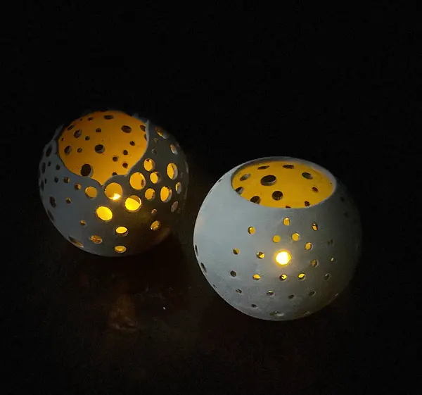 Two white ceramic spherical candle holders with circular pierced patterns glowing from within on a dark background.