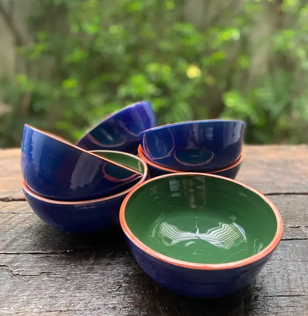 Glossy cobalt blue bowls with dark green interiors and orange rims on a weathered wood surface.