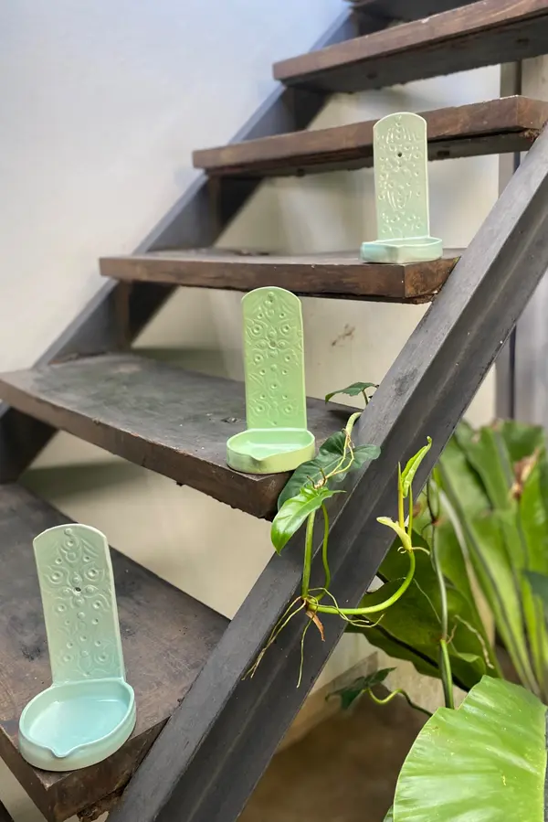Three light green ceramic wall holders with embossed floral patterns arranged on rustic wooden stairs.