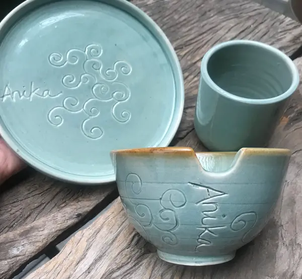 Set of light blue ceramic pottery featuring a plate, bowl, and cup with spiral engravings on a wooden surface.