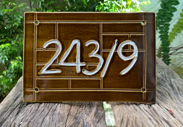 Brown ceramic house number plaque with white embossed digits 243/9 and a grid-like texture.