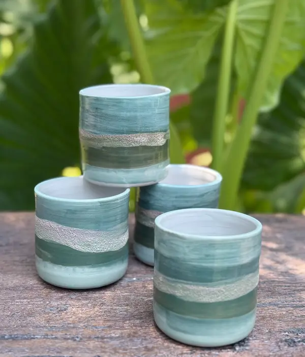 Four cylindrical ceramic tumblers with sage and turquoise banded glazes and a textured silver-toned stripe.