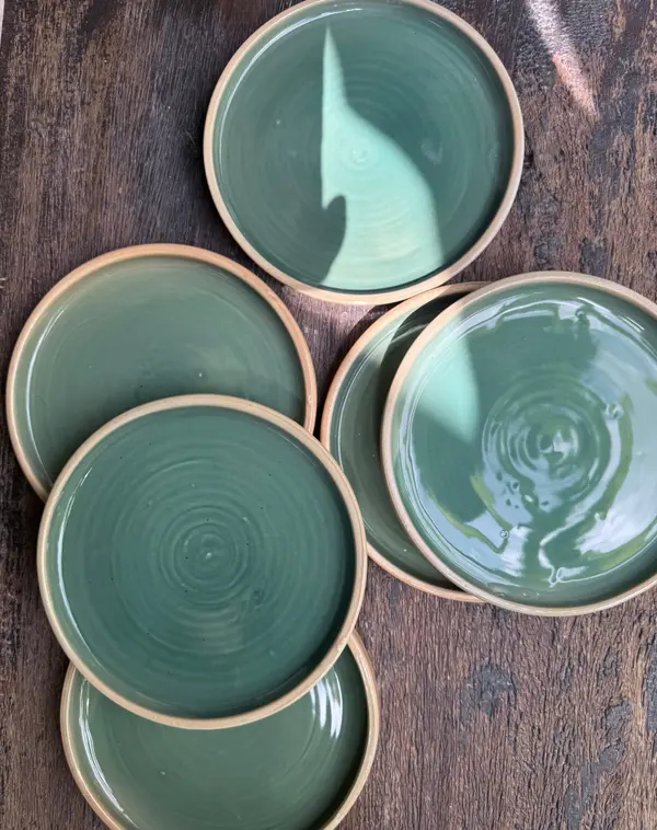 Set of circular dark green glazed ceramic plates with unglazed rims on a textured wood surface.