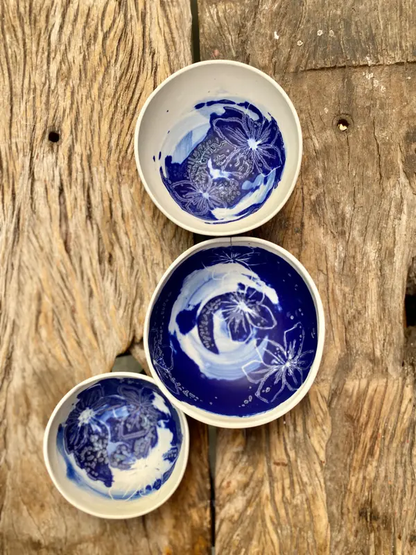 Three white ceramic bowls with cobalt blue floral and brushstroke designs on a rustic wood surface.