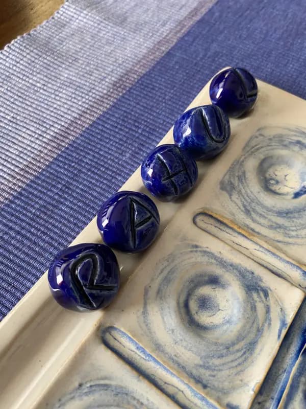 White ceramic board with blue swirls and five cobalt blue marbles featuring etched letters on a blue cloth.