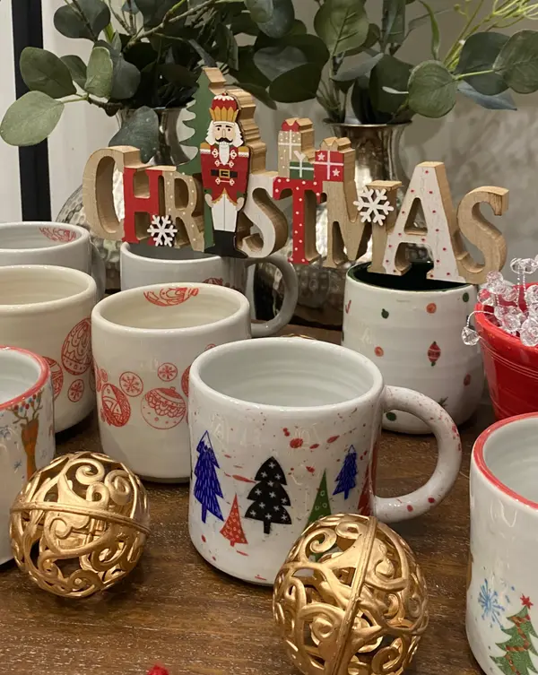 Collection of hand-painted ceramic mugs featuring festive Christmas trees and ornament patterns.