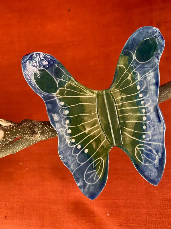 Butterfly-shaped ceramic wall hanging with cobalt blue and green glazes and white line patterns on a branch.