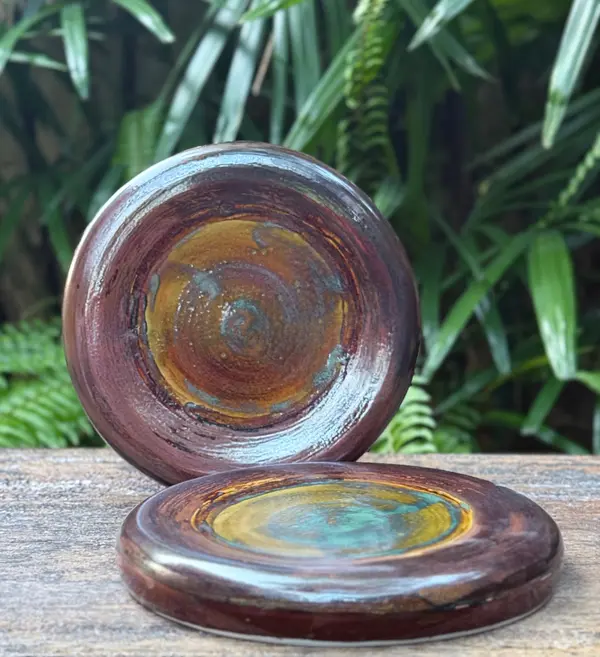 Two circular ceramic coasters with a glossy swirled glaze in dark red, yellow, and turquoise.