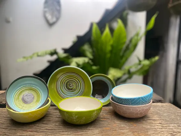 Collection of colorful ceramic bowls with hand-painted swirl and leaf designs on a rustic wooden surface.