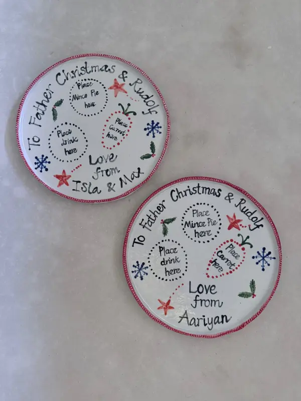Two white ceramic plates for Father Christmas featuring hand-painted red, green, and black holiday illustrations.