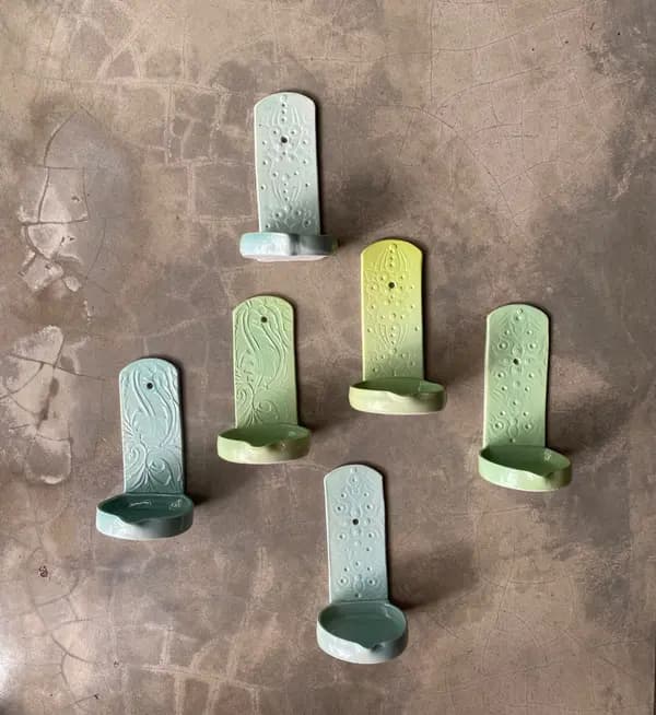 Six wall-mounted ceramic candle holders in mint and sage green glazes with embossed patterns on a concrete surface.