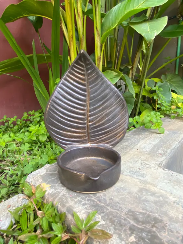 Black metallic pottery candle holder featuring a large sculpted leaf back and a small circular dish.