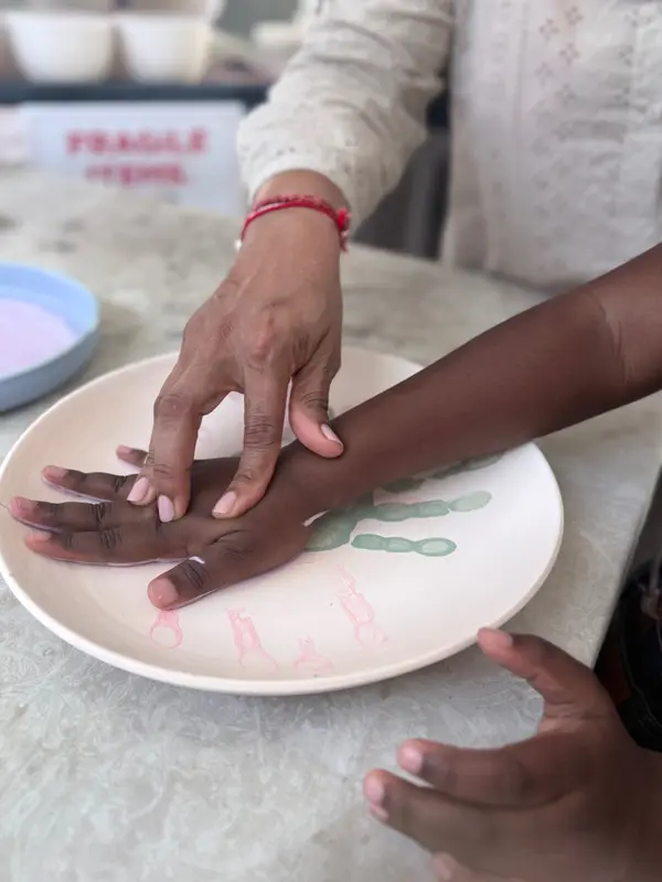 A child's hand being pressed onto a beige ceramic plate to create a handprint keepsake.