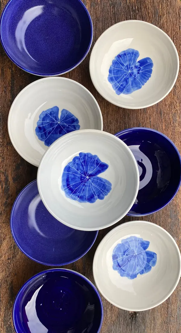 Group of white and cobalt blue ceramic bowls featuring a hand-painted blue lotus leaf design on a wooden table.