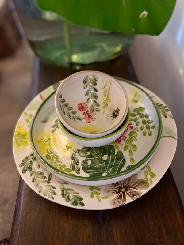 Stacked ceramic plates and nested bowls featuring hand-painted botanical leaves and colorful floral designs.
