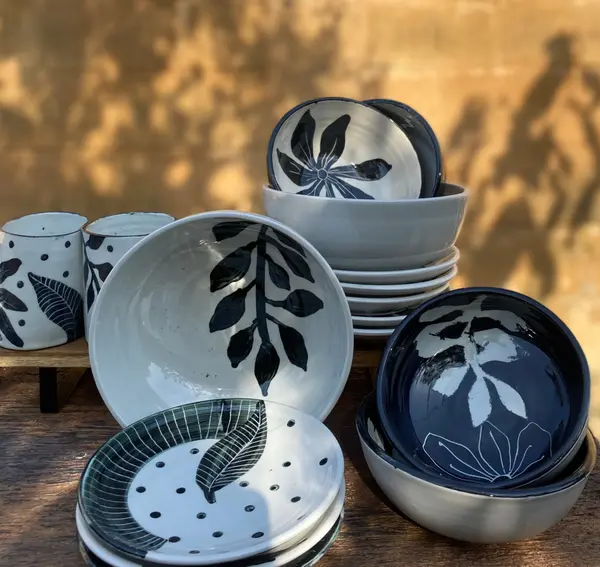 White and black ceramic tableware with hand-painted botanical leaf and dot designs on a wooden table.