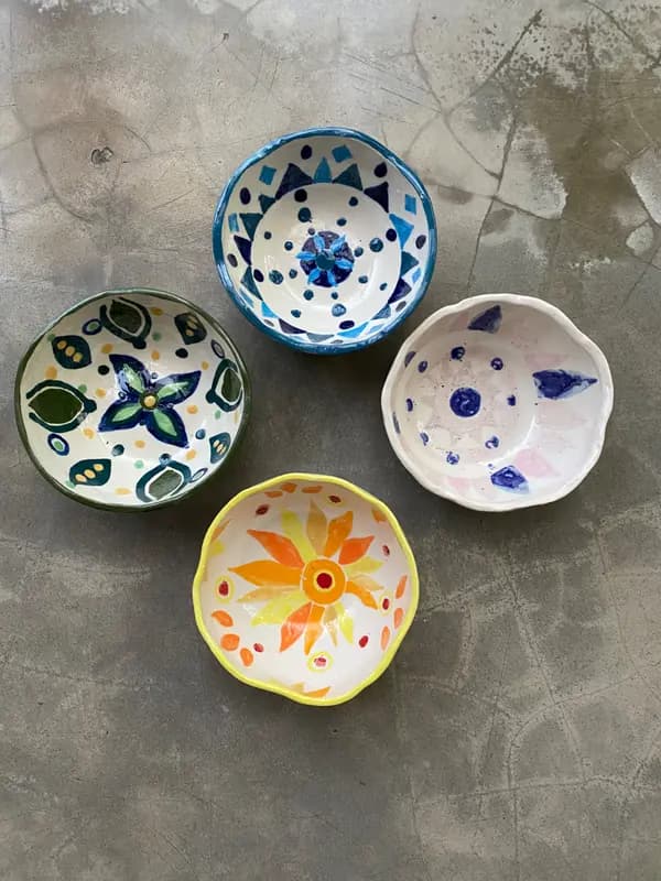 Four hand-painted ceramic bowls with colorful floral and geometric patterns on a gray concrete background.