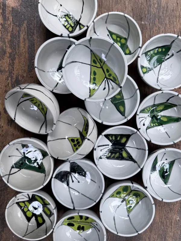 Small white ceramic bowls with hand-painted green and black butterfly motifs arranged on a wooden table.