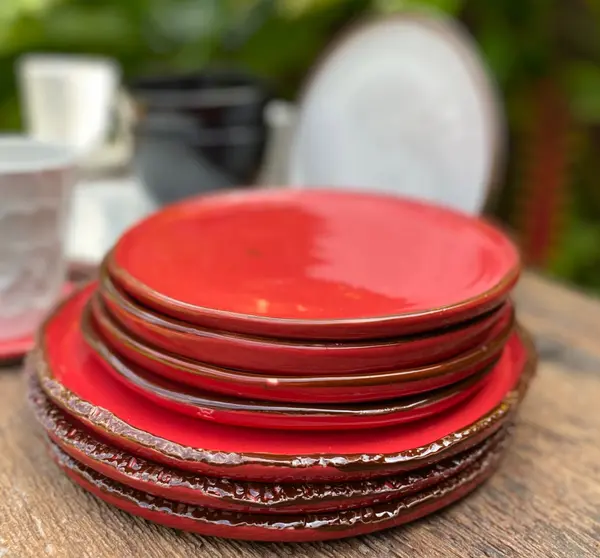 Stack of vibrant red glazed ceramic plates with dark textured rims on a wooden surface.
