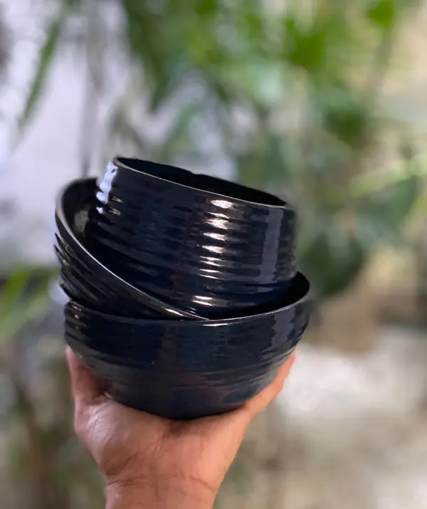 A stack of three ribbed cobalt blue ceramic bowls held in a hand against a blurred green background.