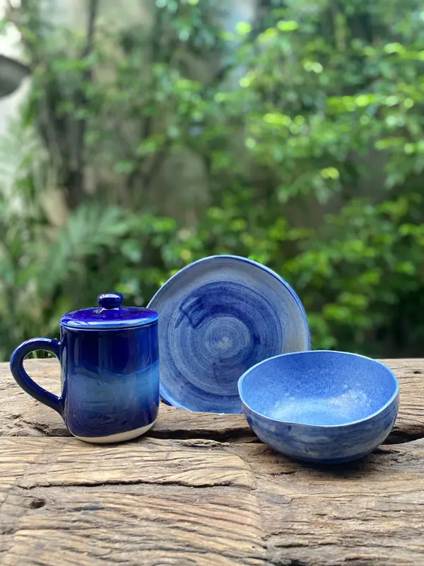 Handcrafted blue ceramic mug, plate, and bowl set with a dark cobalt glaze on a weathered wood table.