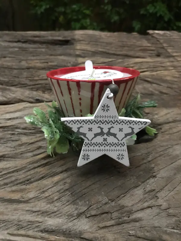 Striped red and white ceramic candle holder with a wooden star ornament and green sprigs on a rustic wood surface.