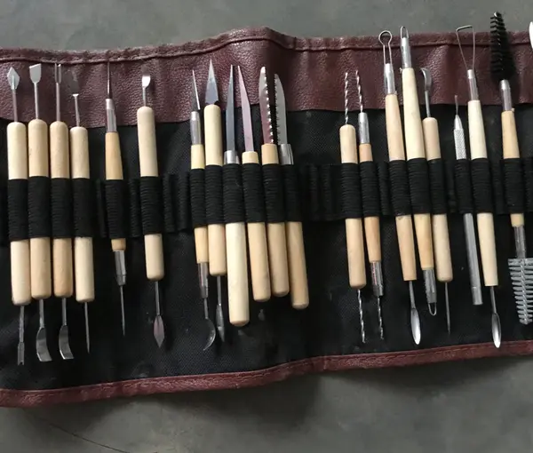 Pottery carving and sculpting tools with wooden handles organized in a brown leather-like roll-up pouch.