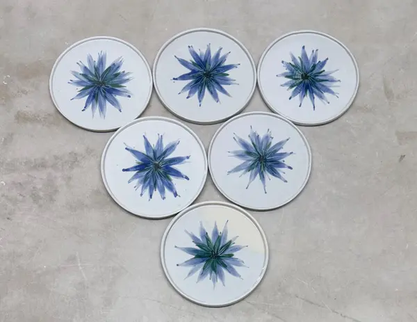 Six white ceramic plates with blue and green floral patterns arranged in a triangle on a gray surface.