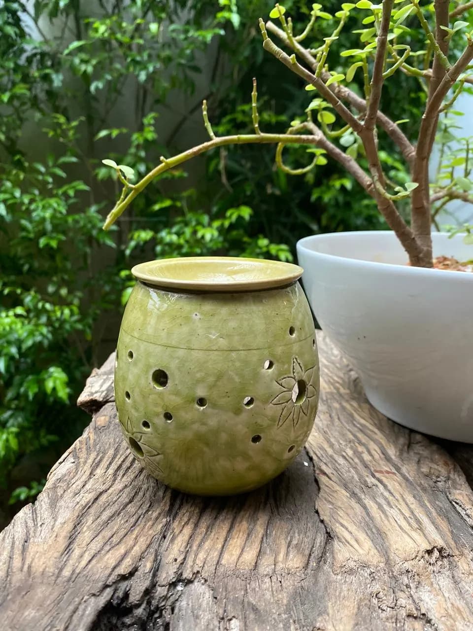 Round light green ceramic candle holder with perforated holes and floral carvings on a wooden surface.