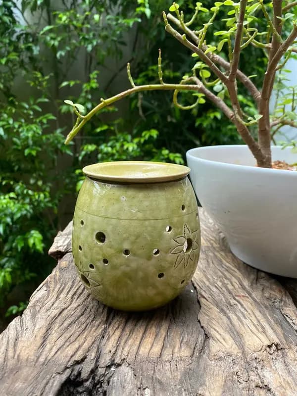 Round light green ceramic candle holder with perforated holes and floral carvings on a wooden surface.