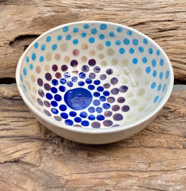 White ceramic bowl with concentric dot patterns in cobalt, purple, and light blue on a rustic wood surface.