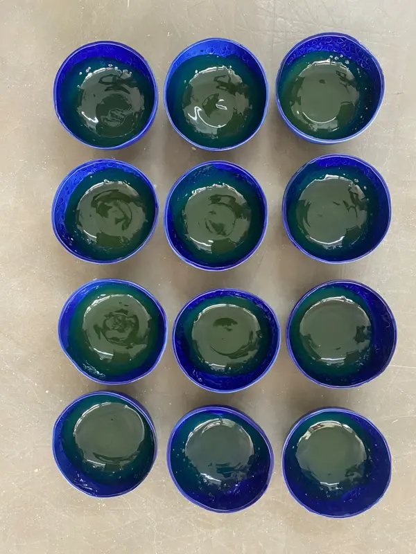 Twelve small ceramic bowls in a grid, featuring cobalt blue exteriors and glossy dark green glazed interiors.